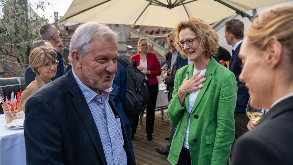 Gäste im lockeren Austausch unter dem Sonnenschirm auf der Dachterrasse